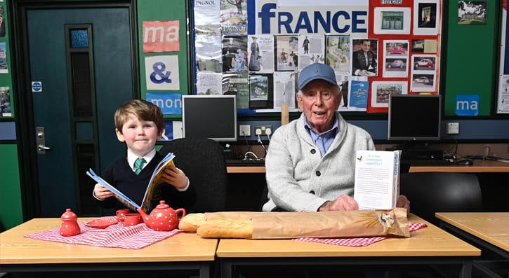 Young child and older man at desk in French class with baguettes, books and picnic